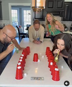 four people sitting around a table with red cups in front of them and one person standing at the end