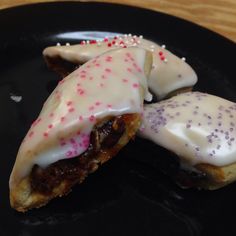 two pastries with white icing and pink sprinkles on a black plate