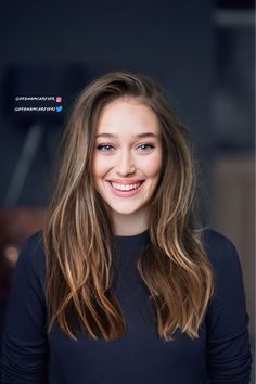 a woman with long hair and blue eyes smiling at the camera while wearing a black top