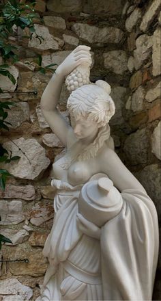 a statue of a woman holding a pot in front of a stone wall with ivy growing on it