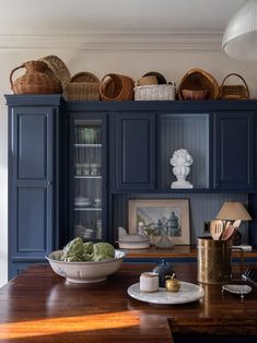 a kitchen with blue cabinets and baskets on the top shelf, along with a bowl of lettuce