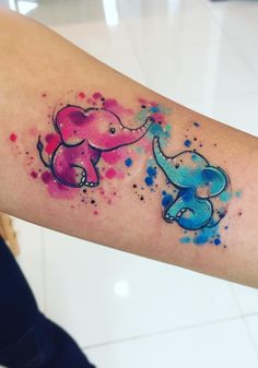 an elephant tattoo on the arm with watercolor splashs around it and two elephants