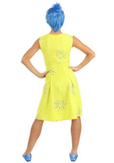 a woman in a yellow dress with blue hair is standing back to the camera and her hands on her hips