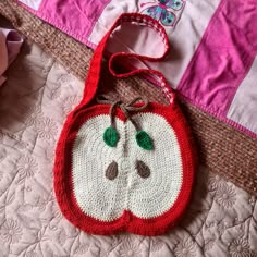 a crocheted apple bag sitting on top of a bed