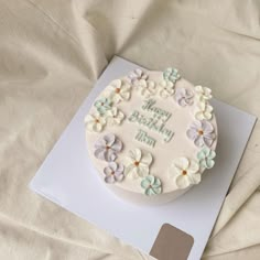 a birthday cake with white frosting and blue flowers on the top is sitting on a sheet