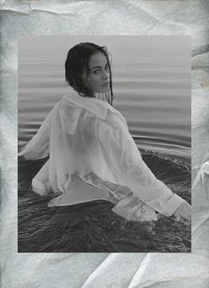 a black and white photo of a woman sitting in the water with her hands on her hips