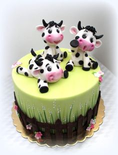 two small cows sitting on top of a green cake