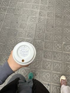 a person holding a white coffee cup in their left hand on the ground with other people's feet