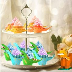 three tiered tray with cupcakes decorated like dinosaurs and one dinosaur is eating