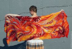 a woman is holding an orange and red shawl over her head while standing in front of a gray wall