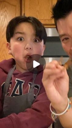 a man and boy making funny faces while eating food in front of the kitchen counter