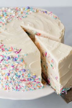 a cake with white frosting and sprinkles on a plate next to a knife