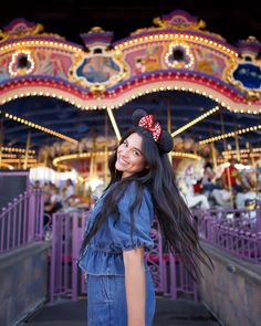 a woman standing in front of a merry go round at an amusement park with her long hair blowing in the wind