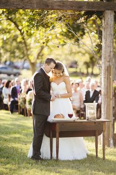 a bride and groom standing in front of a table with wine glasses on it at their wedding ceremony