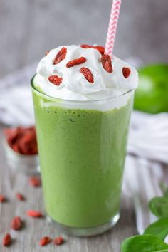 a green smoothie with whipped cream and sunflower seeds on the rim, garnished with a pink striped straw