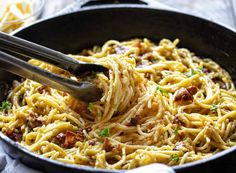 spaghetti being cooked in a skillet with tongs