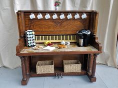 an old wooden organ with coffee cups and other items on the top, sitting in front of a white curtain