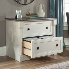 a white dresser with two drawers and a clock on the wall in front of it