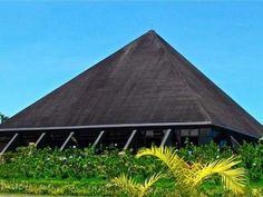 a building with a triangle shaped roof next to trees and bushes