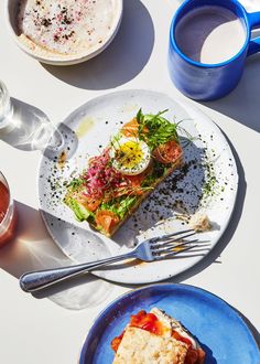 two plates with food on them next to cups and saucers, one has a slice of pizza