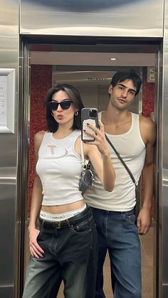 a man and woman taking a selfie in front of an elevator door with their cell phone