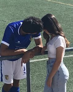 a man and woman standing next to each other on top of a soccer field near a fence