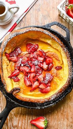 a skillet with strawberries and powdered sugar in it on a wooden table