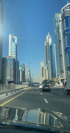 cars driving down the road in front of tall buildings with skyscrapers on either side