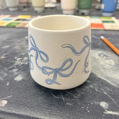 a cup sitting on top of a table next to some paintbrushes and markers