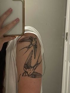 a woman with a bird tattoo on her arm holding up a mirror to take a photo