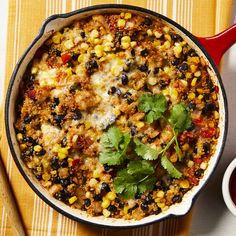 a red skillet filled with mexican food next to a bowl of sauce and a spoon