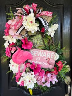 a pink flamingo wreath on a black door with beware of the flamingos sign