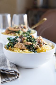 two white bowls filled with food sitting on top of a table next to silverware