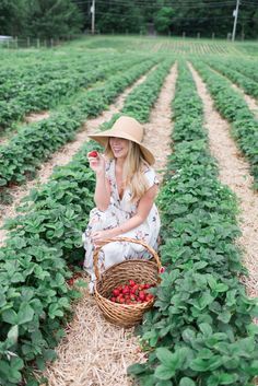 a woman in a straw hat sitting on the ground holding a basket with strawberries