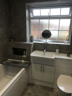 a bath room with a toilet a sink and a tub next to a window in it