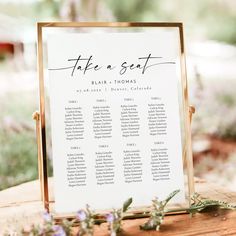 a wooden table with a sign that says take a seat on it and flowers in the background