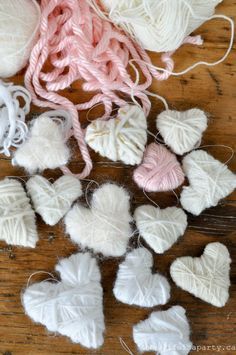 some white and pink hearts are sitting on a wooden table next to yarn, scissors and thread