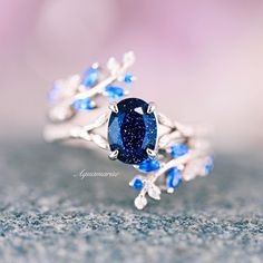 a close up view of a ring with a blue stone in the center and leaves on it