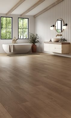 a large bathroom with white walls and wood flooring is pictured in this image, there are two sinks on either side of the bathtub