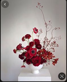 a white vase filled with red flowers on top of a table