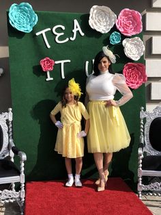 two women standing next to each other in front of a wall with flowers on it