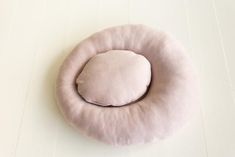 a pink pillow sitting on top of a white floor next to a wooden table with an object in the middle