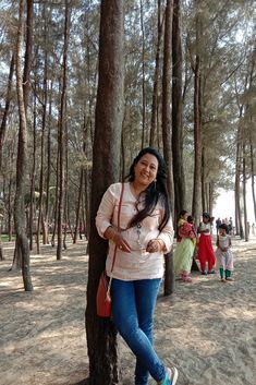 a woman standing next to a tree in a forest with other people behind her smiling