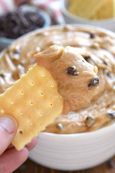 a hand holding a cracker over a bowl of peanut butter and chocolate chip dip