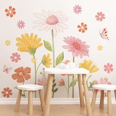 a table and two stools in front of a wall with flowers painted on it