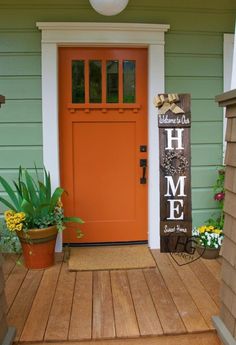 an orange front door with the words home on it and potted plants in front