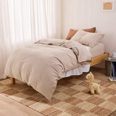 a bed with two pillows and a stuffed animal on the floor in front of it