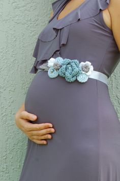 a pregnant woman wearing a purple dress and flower belt