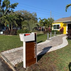 a mailbox in front of a yellow house with palm trees and bushes around it