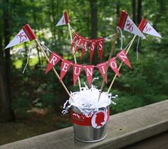 a bucket filled with red and white flags sitting on top of a wooden deck next to trees